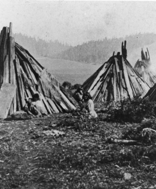 Historic indigenous dwellings with people and hills.